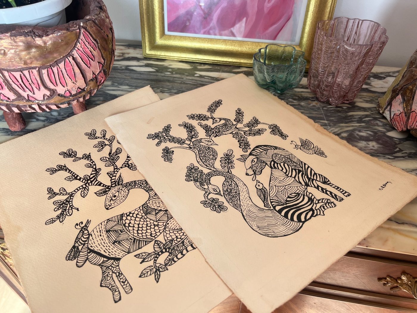 Two Gond style ink drawings of a deer and a peacock with trees and birds, on handmade paper